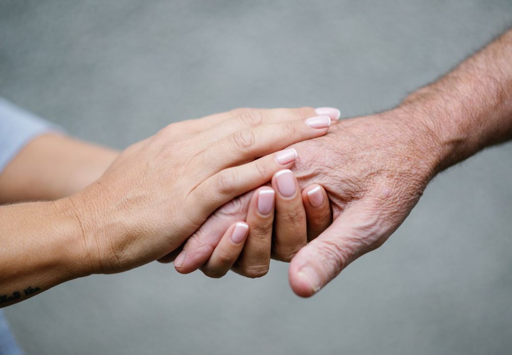 A younger pair of hands gently holding an older person's hand.